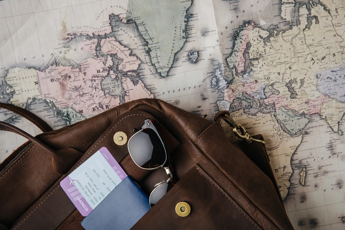 A brown travel bag, sunglasses and travel documents on a vintage-style map.