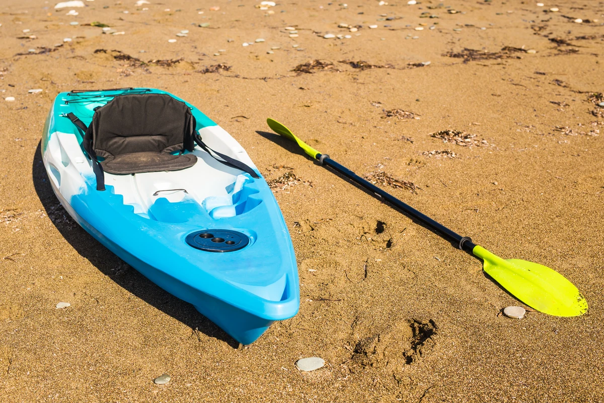 A blue kayak and a yellow-green paddle resting on sand.