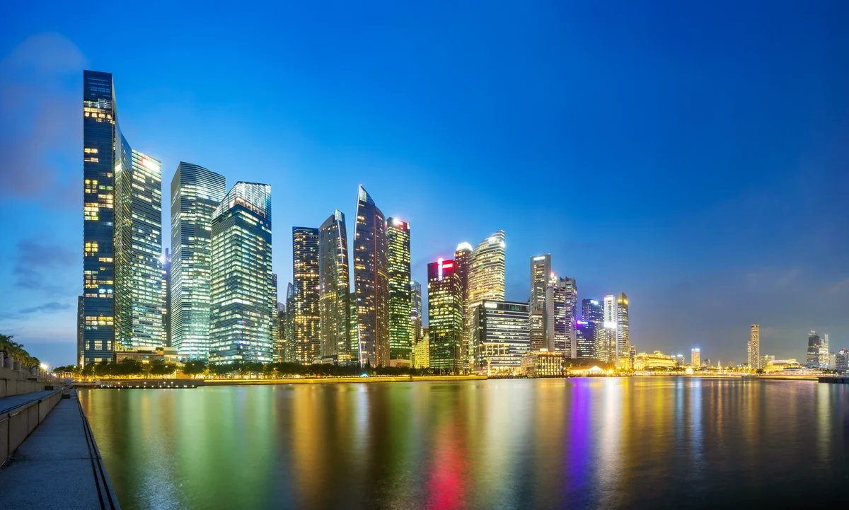Panoramablick auf Singapurs Marina Bay in der Abenddämmerung als illustrative Stadtansicht.